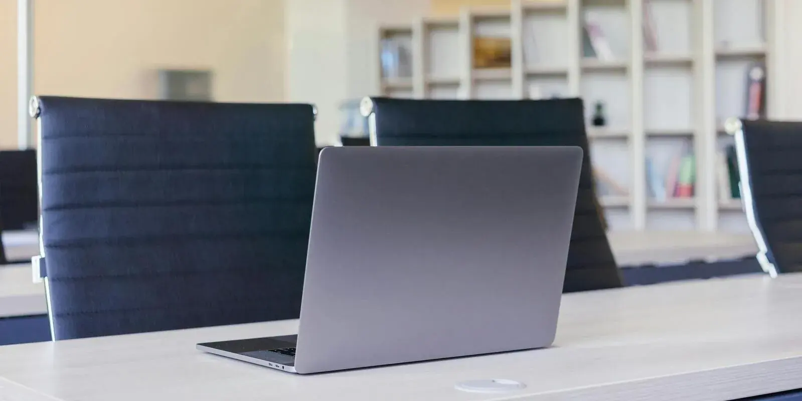 A laptop open on a boardroom table in a professional office with leather chairs and bookshelves