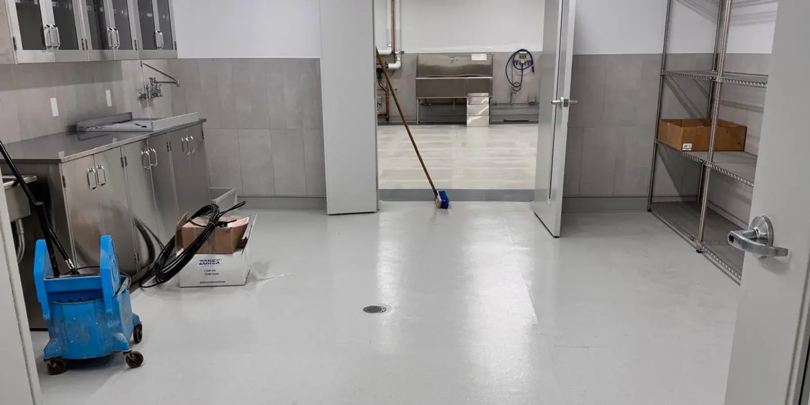 A finished commercial kitchen with stainless casework, tiled walls, and a prep room beyond