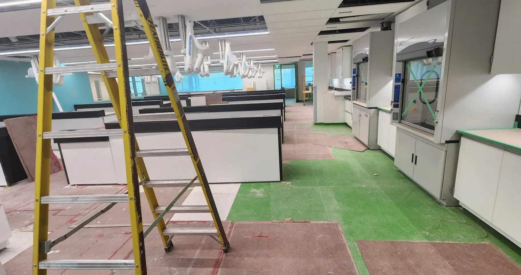 A newly built commercial interior mid-fit-out with a ladder, casework, and protective floor covering