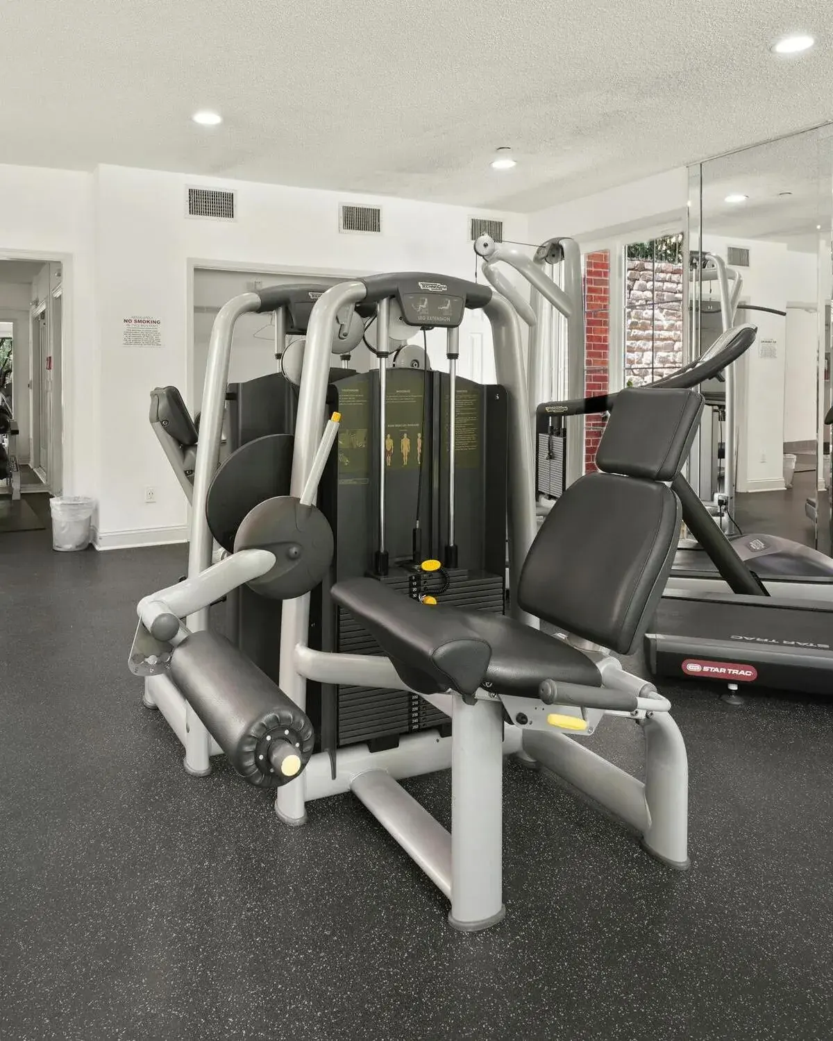 A fitness facility with a strength-training machine and a treadmill on rubber gym flooring