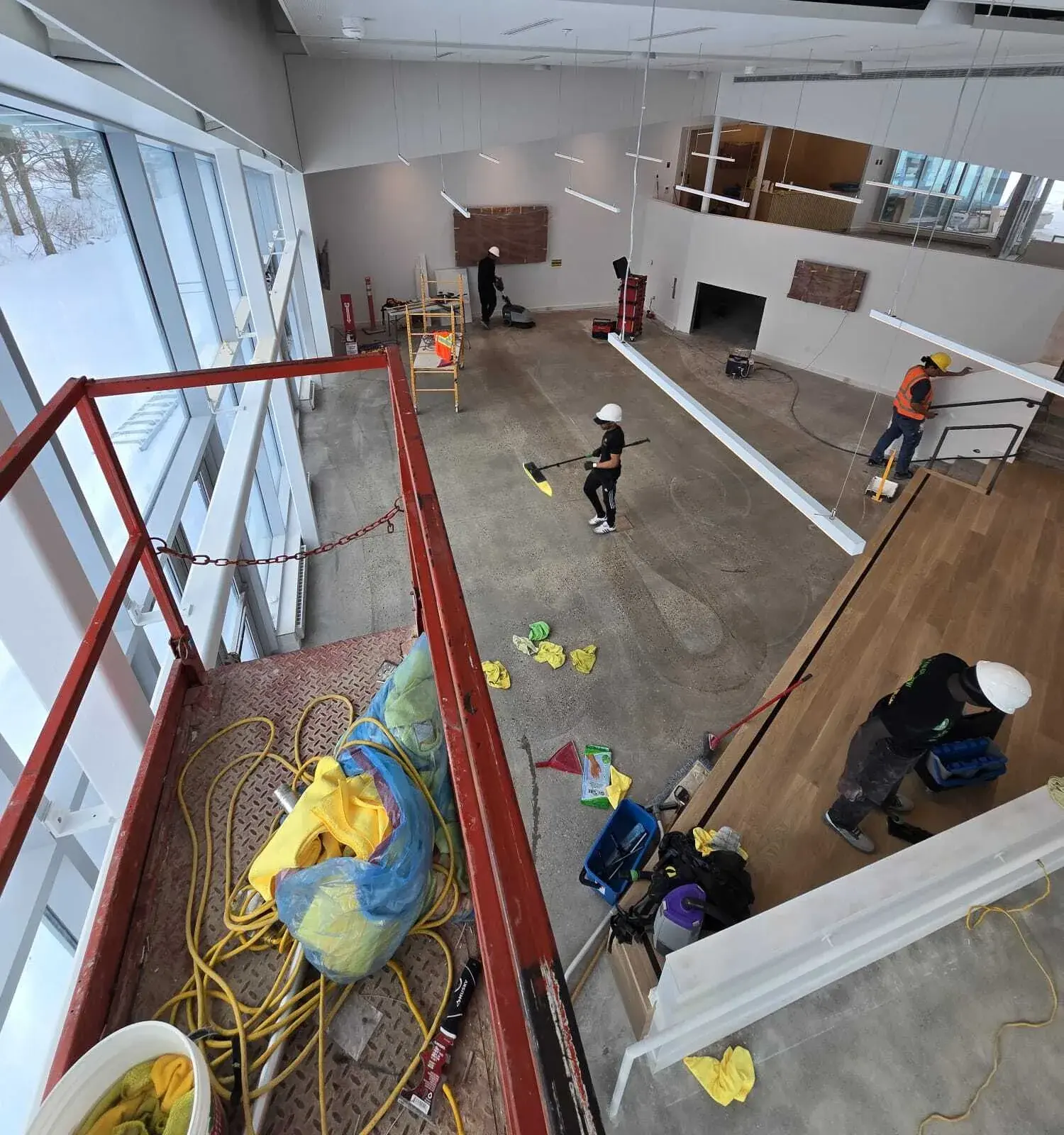 Overhead view of a cleaning crew in hard hats clearing and cleaning a large open commercial space during a post-construction job