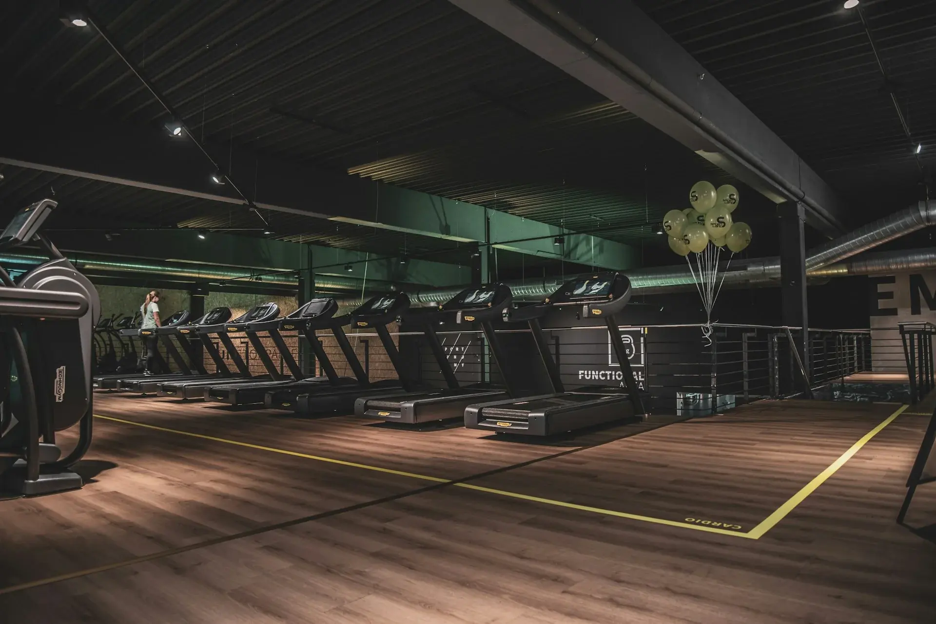 A dark, modern commercial gym with a long row of treadmills and cardio machines under moody lighting