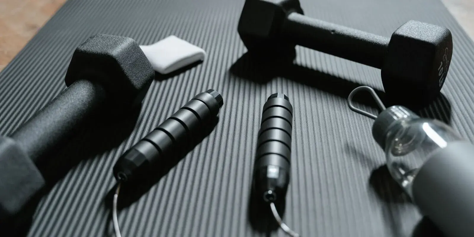 Dumbbells, a skipping rope, a towel, and a water bottle arranged on an exercise mat