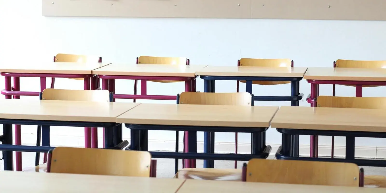 Rows of empty wooden desks and chairs in a classroom