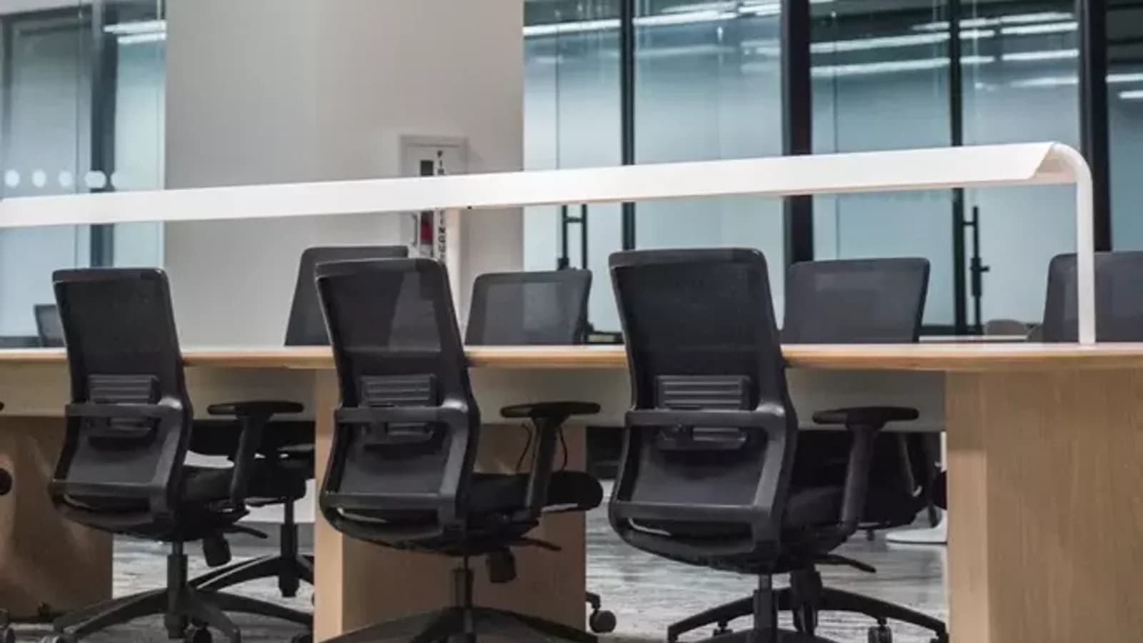 A clean, modern open-plan office with rows of mesh task chairs and wooden desks