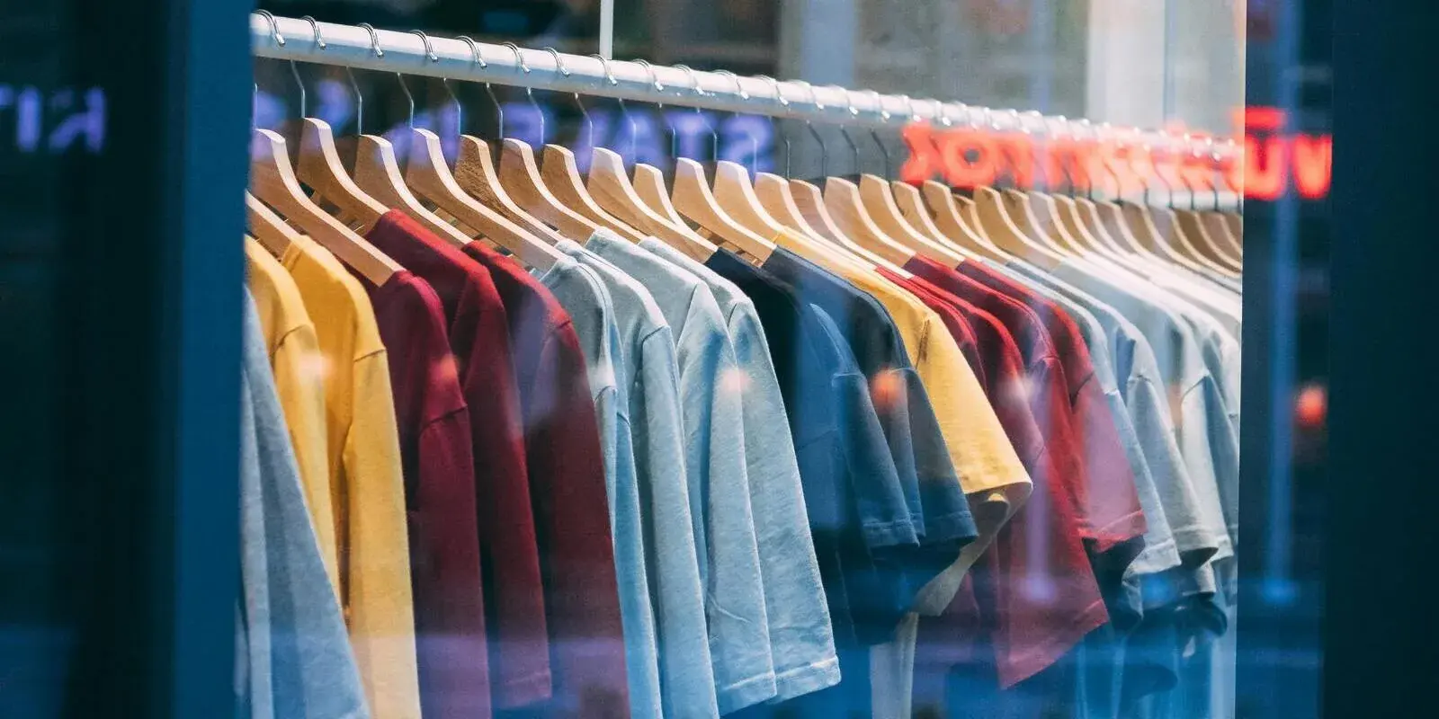 A retail storefront display window showing a rack of colourful shirts behind clean glass
